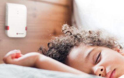 Person sleeping with a white electronic device on the wall above them